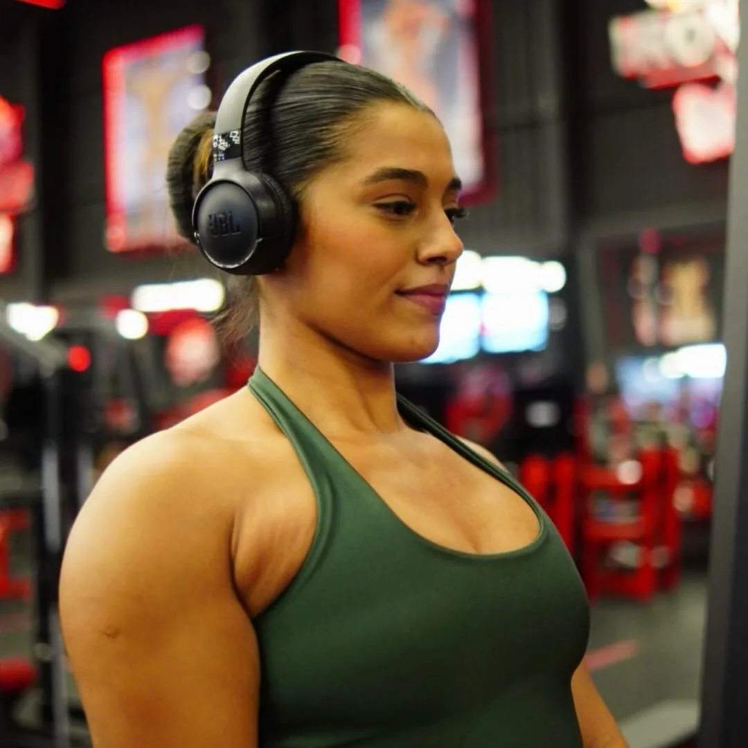 Thaina Marceiro de fone de ouvido JBL preto, regata verde, na academia